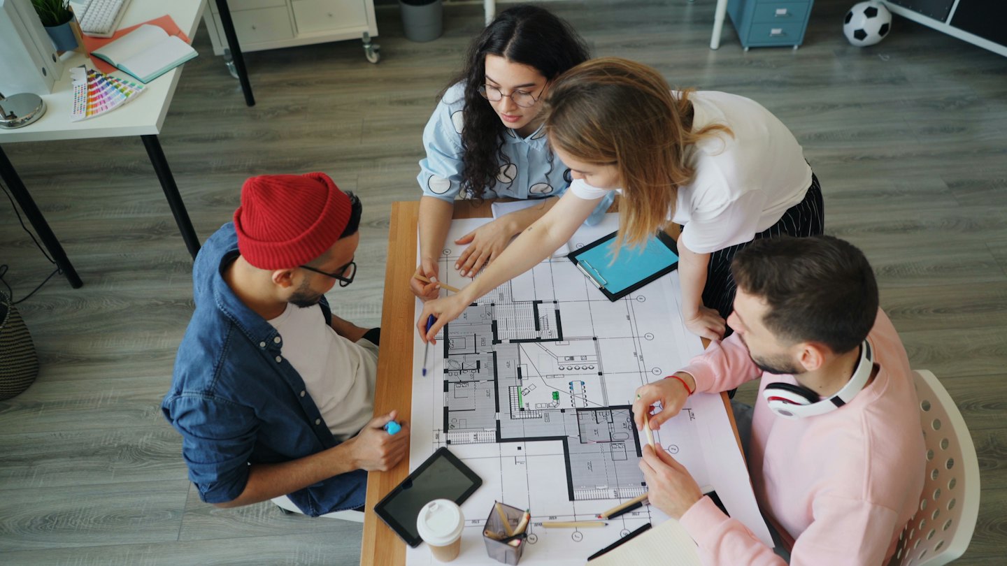 Quattro designer collaborano su un progetto architettonico su un tavolo.